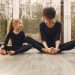 Anonymous mother in sportswear sitting near smiling little blond daughter with crossed legs on parquet while looking at each other in daylight